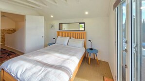 A bedroom with a bed, a nightstand, a mirror, and a view through a glass door.