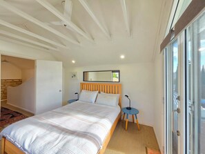 Une chambre à coucher avec un lit, une table de chevet, un miroir et une vue sur l’extérieur, visible à travers une porte vitrée.