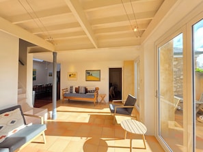 Un espace de vie spacieux comprenant un canapĂ©, des fauteuils, une petite table et une vue dĂ©gagĂ©e sur lâextĂ©rieur grĂące Ă une porte vitrĂ©e.
