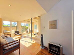 Un salon moderne avec un canapé, des fauteuils, un radiateur et une vue sur l’extérieur, accessible par des portes vitrées.