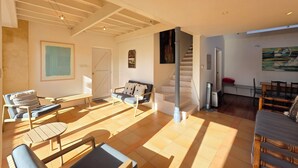 A spacious living area with a sofa, chairs, a dining table, and a staircase leading to another level.