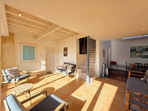 Un grand espace de vie comprenant un canapé, des fauteuils, une table à manger et un escalier menant à un autre niveau.