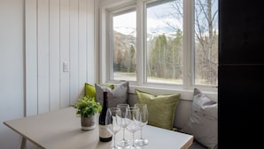 A room with a window overlooking a mountainous landscape, a table with a bottle and glasses, and a potted plant.