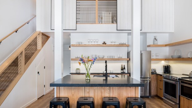 A modern kitchen with a central island, wooden cabinets, stainless steel appliances, and a staircase with wooden railings.