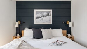 A neatly arranged bedroom with a bed, pillows, a framed picture on the wall, bedside lamps, and a magazine on the bed.