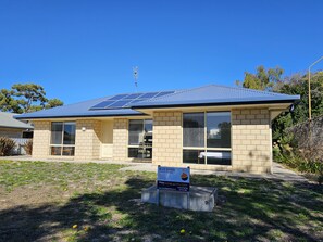 Two-story building with a flat roof and solar panels, set amidst a lush lawn with flowers and trees.
