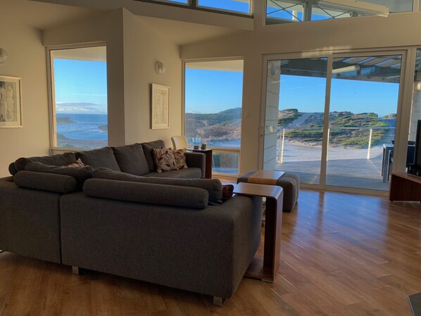 Relax in this stylish living room with a large sofa and coffee table, offering breathtaking views of the coastal landscape.