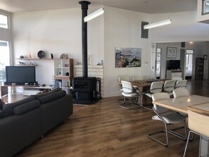 Cozy living space with a central stove, sofa, dining area, and large window.
