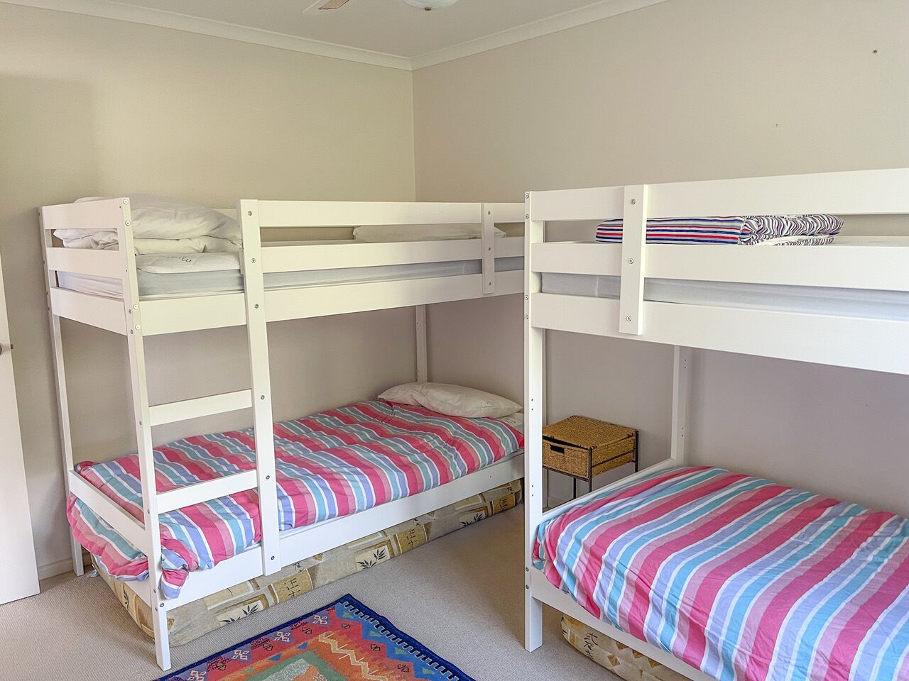 Ein Zimmer mit zwei Etagenbetten, jeweils mit einer gestreiften Bettdecke. Auf dem Boden steht eine kleine Holzkommode und ein gewebter Korb.