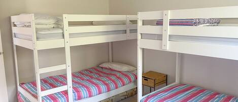 Ein Zimmer mit zwei Etagenbetten, jeweils mit einer gestreiften Bettdecke. Auf dem Boden steht eine kleine Holzkommode und ein gewebter Korb.