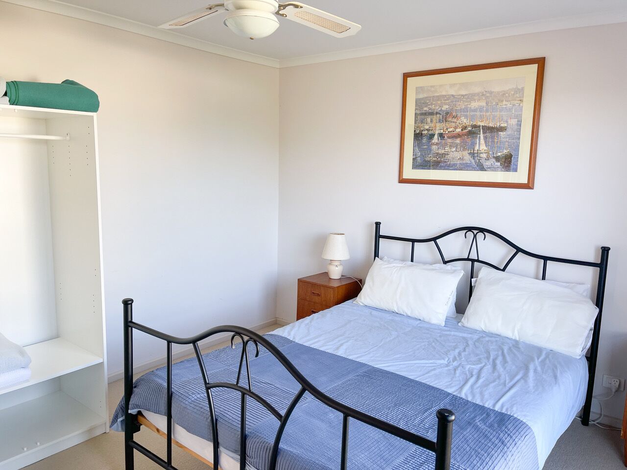 A bedroom with a bed, a nightstand, a chair, a wardrobe, and a ceiling fan.