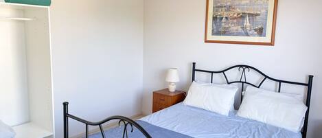 A bedroom with a bed, a nightstand, a chair, a wardrobe, and a ceiling fan.