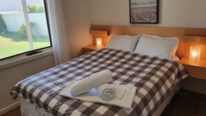 A neatly made bed with a checkered bedspread, two bedside lamps, and a framed picture on the wall. - Latitude 37 - Large expansive deck - Pets Welcome - Outside Only (Robe)