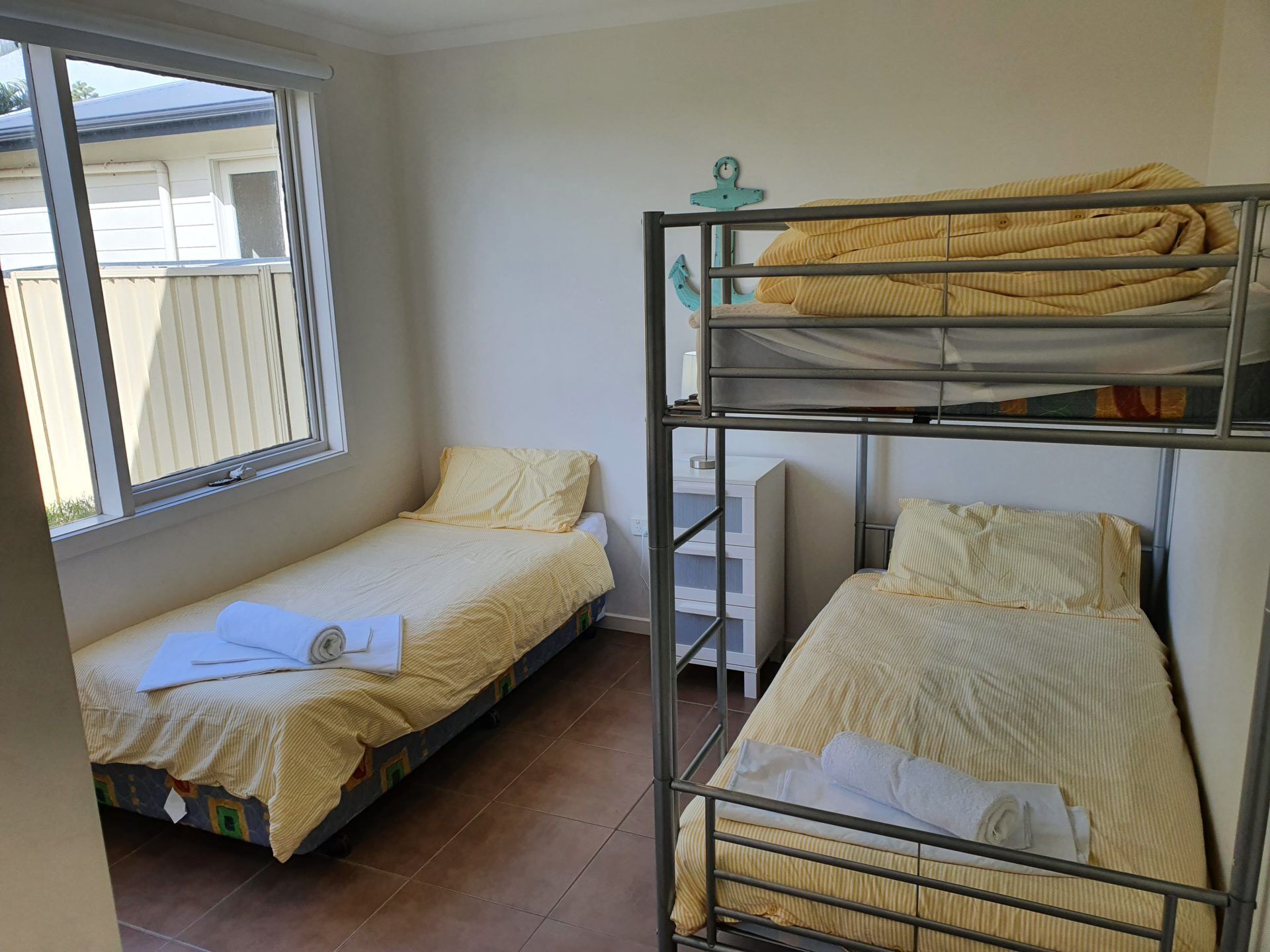 A dormitory room with two single beds and a bunk bed, each with striped bedding.
