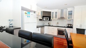 A modern kitchen with white cabinets, a microwave, and a stove. There is a dining area with a wooden table and black chairs. - Latitude 37 - Large expansive deck - Pets Welcome - Outside Only (Robe)