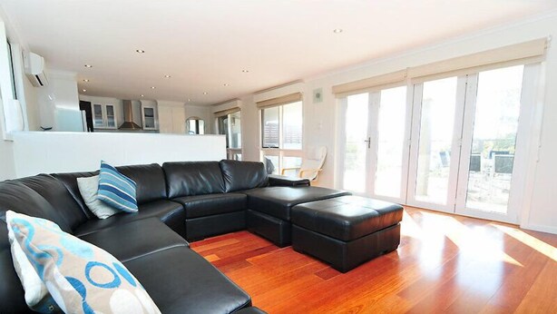 A modern living room with a black leather sectional sofa, a wooden floor, and large windows offering a view of the outside. - Latitude 37 - Large expansive deck - Pets Welcome - Outside Only (Robe)