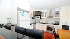 A modern kitchen with white cabinets, a microwave, and a stove. There is a dining area with a wooden table and black chairs.