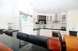 A modern kitchen with white cabinets, a microwave, and a stove. There is a dining area with a wooden table and black chairs.