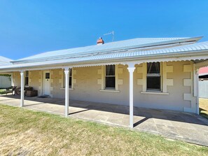 A single-story building with a corrugated metal roof, a porch with white columns, and a small attached garage. - Stone Cottage - Gorgeous cottage charm, in the heart of Robe Town (Robe)