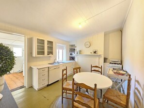 A compact kitchen with white cabinets, a dining table with chairs, a stove, and a clock on the wall. - Stone Cottage - Gorgeous cottage charm, in the heart of Robe Town (Robe)
