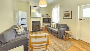 Un salon avec une cheminée, deux canapés, un fauteuil en bois, un téléviseur et une porte avec une fenêtre.