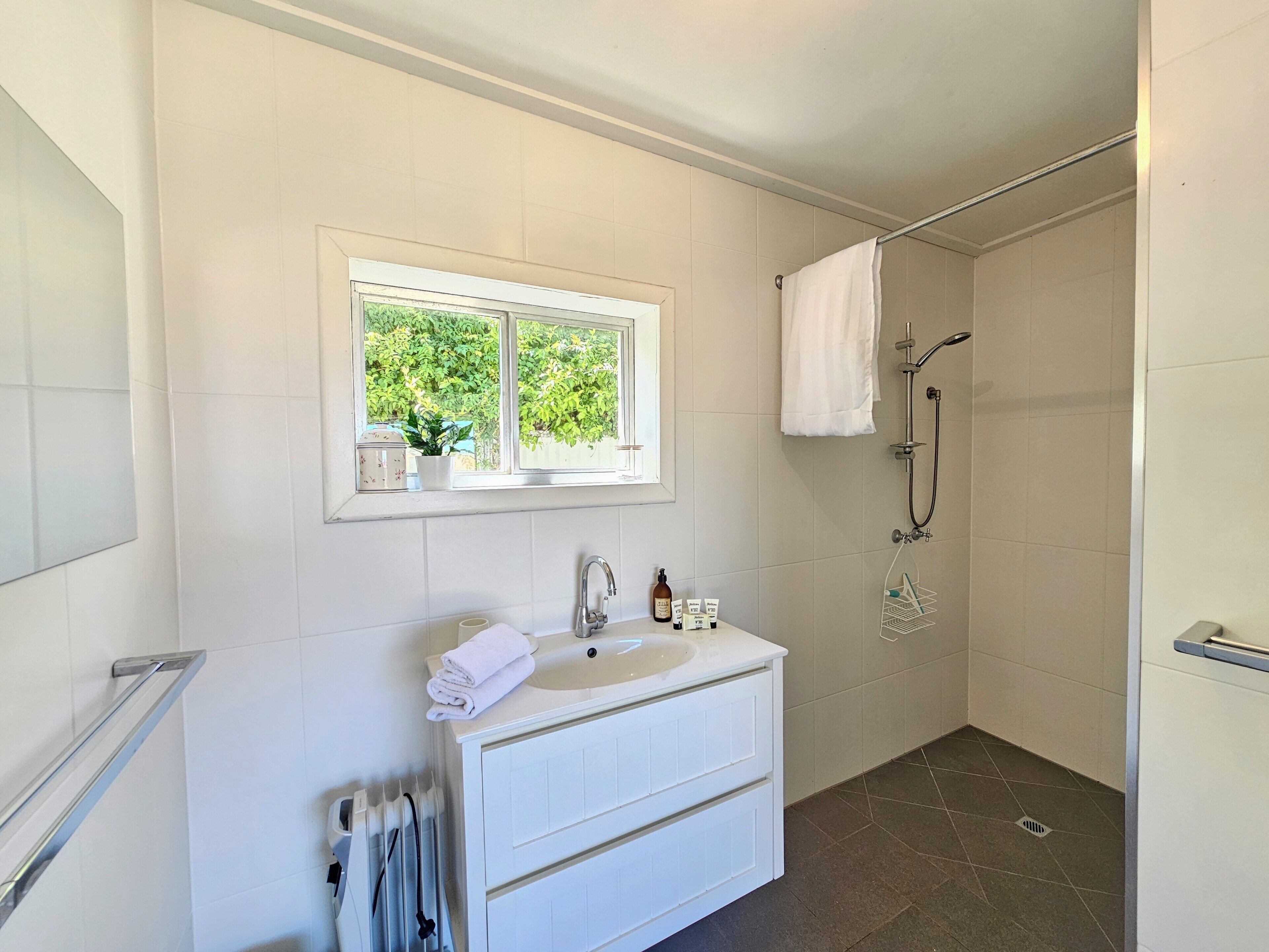 Ein Badezimmer mit weißem Waschtisch, einem Fenster, einer Dusche und einem Handtuchhalter.