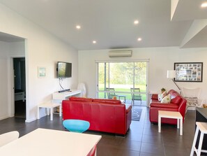 A modern living room with a red sofa, a blue chair, a white table, and a TV on a white stand. - Sun on Sanders - Modern 2 br house close to main street. Pet Friendly Outside (Robe)
