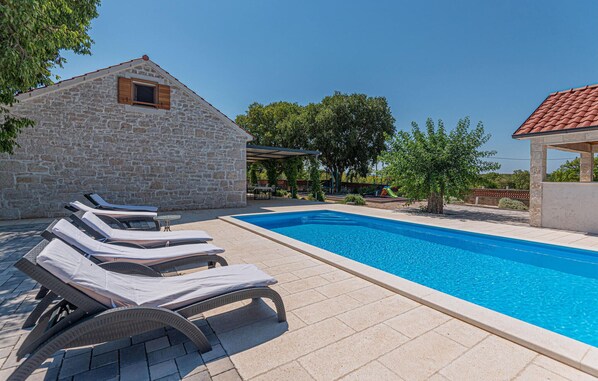 A swimming pool with lounge chairs, a stone building, and a covered area with a table and chairs. - Pet friendly home in Pakovo Selo (Pakovo Selo)