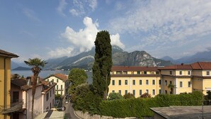 A coastal town with a prominent tall tree, a row of yellow buildings, and a mountain backdrop. - LUCIA by KlabHouse-Central  lakeview w/AC  (Bellagio)