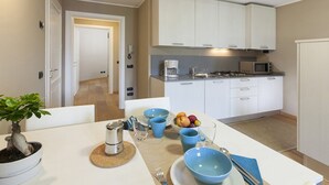 A modern kitchen with white cabinets, a microwave, and a coffee maker. There is a dining table with blue bowls and a fruit bowl. - LUCIA by KlabHouse-Central  lakeview w/AC  (Bellagio)