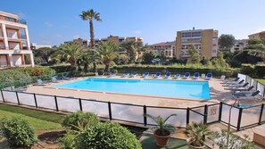 A swimming pool with lounge chairs, surrounded by greenery and buildings. - Apartment for 4 people - Swimming pool - Air conditioning - WiFi - Sainte Maxime (STE MAXIME)