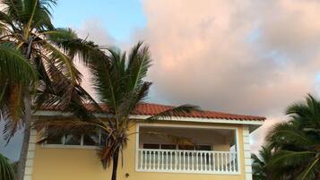 A two-story building with a balcony, a swimming pool, and palm trees.