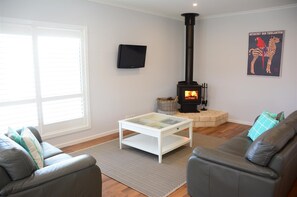 A living room with a fireplace, leather sofas, a glass coffee table, and a flat-screen TV. - Bells On Frome - Coastal shutters, wood fire and the coastal charm. (Robe)