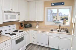 Une cuisine avec des meubles blancs, une cuisinière, un four à micro-ondes et un lave-vaisselle.