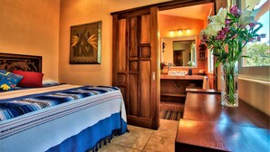 Un dormitorio con cama, puerta de madera, espejo y un jarrón con flores.