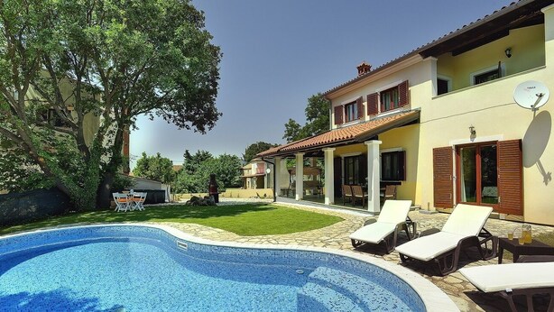 A swimming pool with lounge chairs, a covered patio, and a house with a satellite dish. - Comfortable villa with private pool near sandy beach (Medulin)