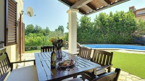 An outdoor patio with a table set for dining, a pool in the background, and a garden area. - Comfortable villa with private pool near sandy beach (Medulin)