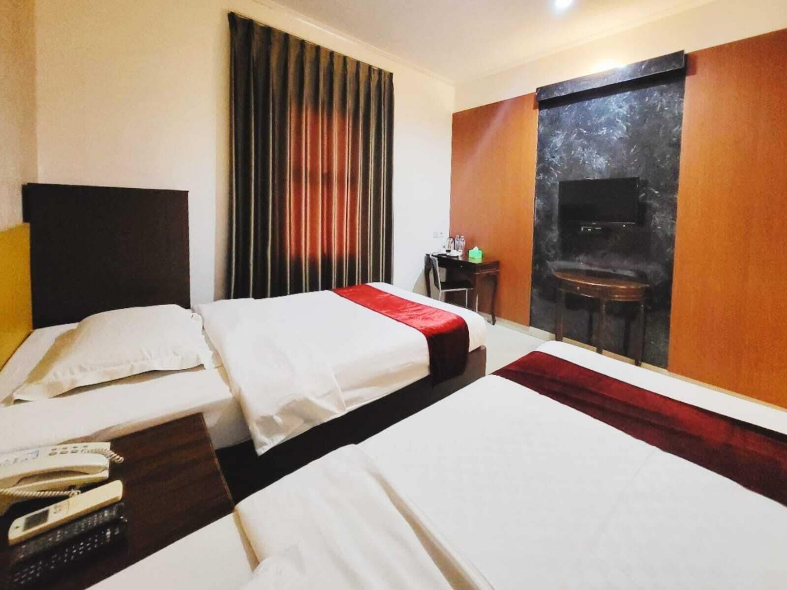A hotel room with two beds, a desk with a chair, a television, and a large window with curtains.