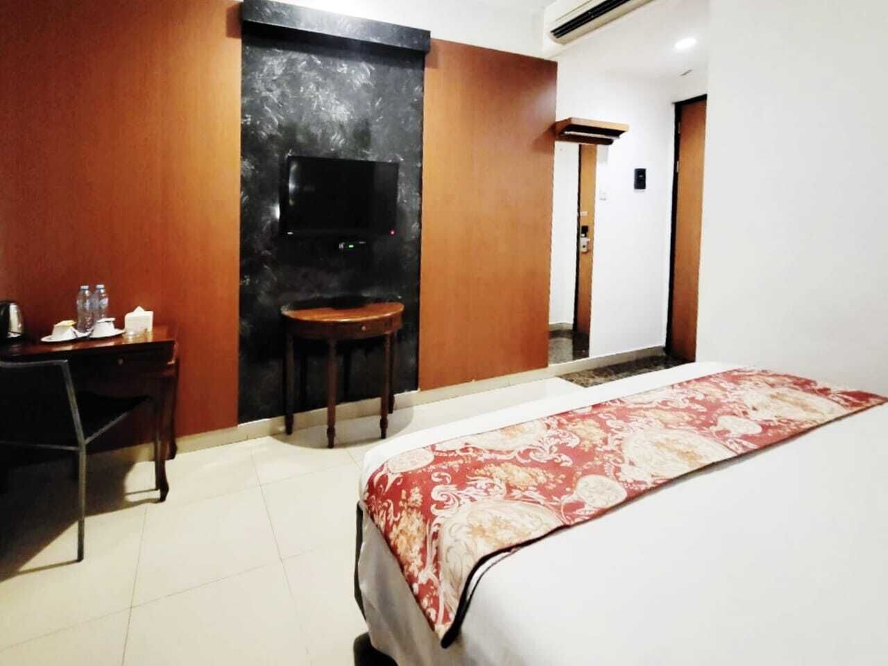 A hotel room with a bed, a desk, a chair, a TV, and a small table.