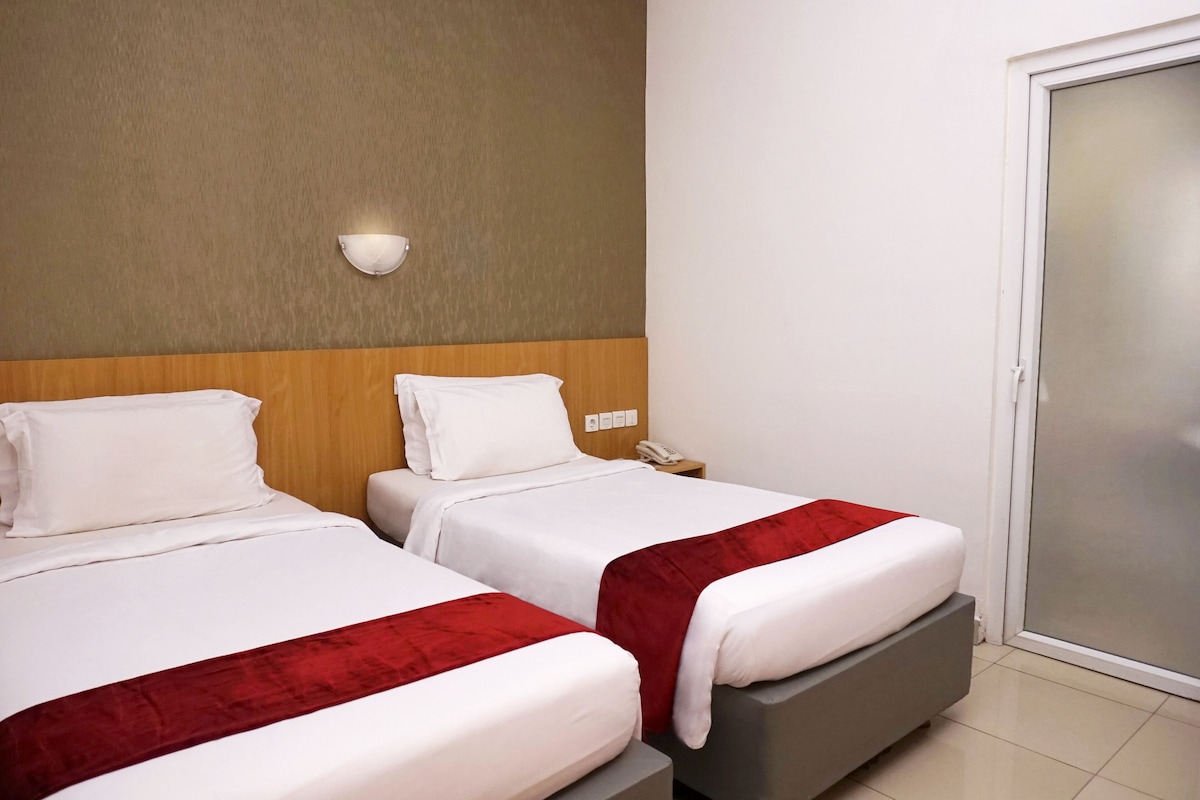 A hotel room with two beds, a wooden headboard, a wall-mounted light, a phone on the nightstand, and a sliding door.