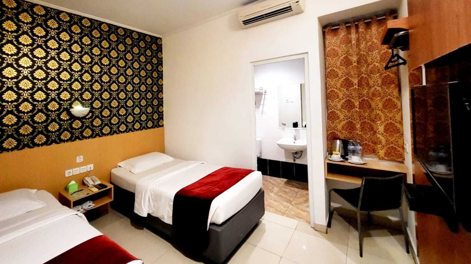 Quarto de hotel com duas camas, uma escrivaninha e uma cadeira. Banheiro visível através de uma porta aberta.