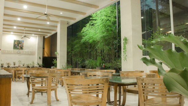 Un restaurante con sillas y mesas de madera, un mural grande en la pared con un bosque, y ventiladores de techo.