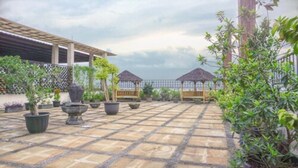 Un patio con suelo de baldosas, plantas en macetas y una pérgola de madera.