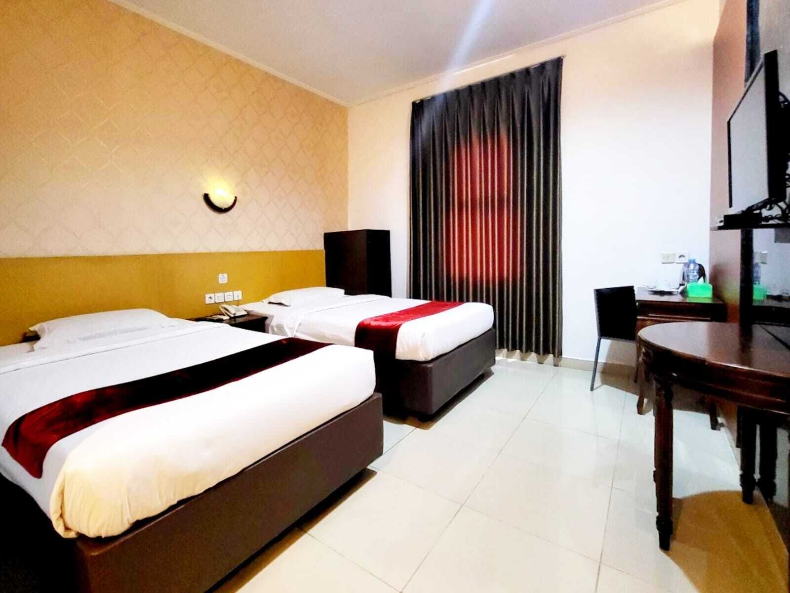 Quarto de hotel com duas camas, uma escrivaninha, uma cadeira, uma televisão e uma janela com cortinas.