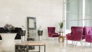 Un salón moderno con un jarrón blanco grande, una mesa de centro de cristal y dos sillones morados.