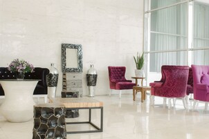 Uma sala de estar moderna com um vaso branco grande, uma mesa de centro de vidro e duas poltronas roxas.
