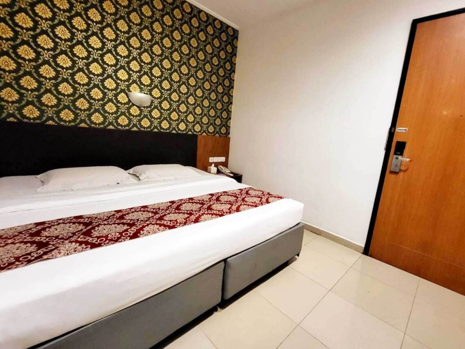 Une chambre d’hôtel avec un lit, une table de chevet, un téléphone et une porte.