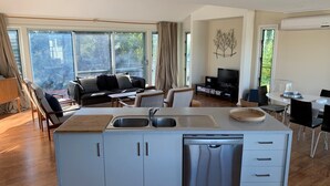 A modern kitchen with a dishwasher, a dining area with a table and chairs, a sofa, and a TV. - Blauhaus - Relax all your blues away... (Robe)