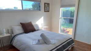 A neatly made bed with a striped bedspread, a brown pillow, and a rolled towel on top. There is a small round rug under the bed, and a wooden crate to the right. - Blauhaus - Relax all your blues away... (Robe)