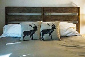 Una cama con cabecera de madera y dos almohadas con diseños de ciervo.
